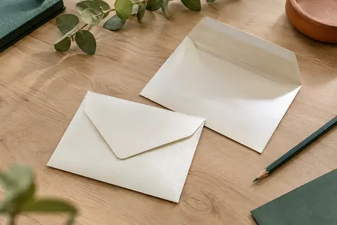Enveloppes C6 ivoire irisées en papier épais, posées sur une table en bois clair