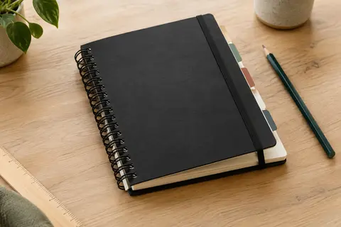 Répertoire téléphonique noir à double spirale et fermeture élastique, ouvert sur une table en bois clair